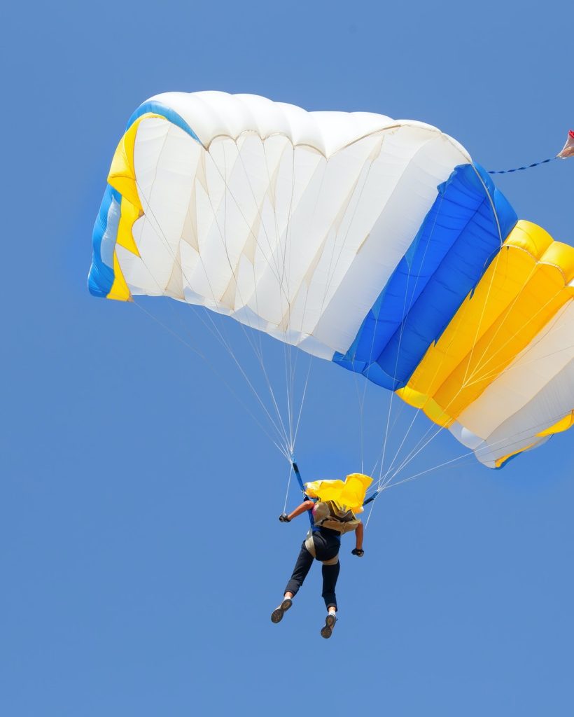skydiver-under-canopy-of-yellow-with-blue-parachute-in-cloudless-sky.jpg